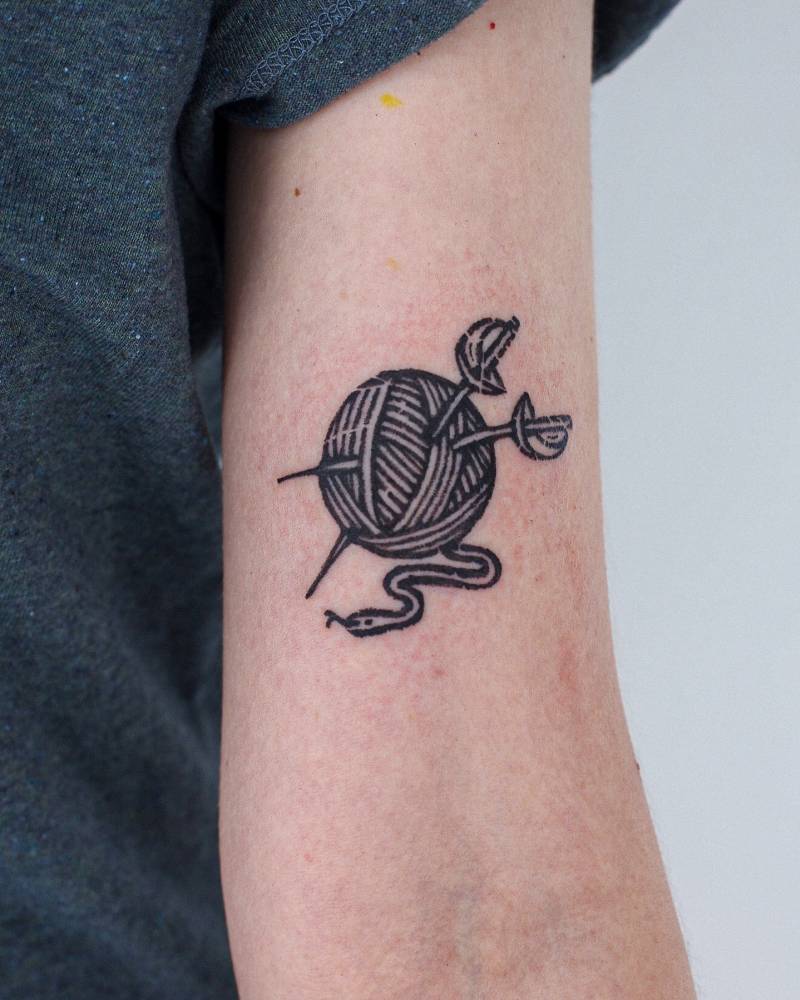Wool yarn and swords tattooed on the bicep, blackwork style.