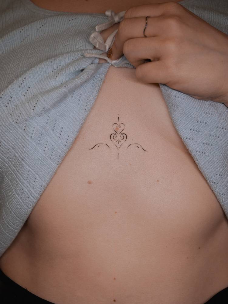 Fine line style ornamental heart tattoo located on the sternum.