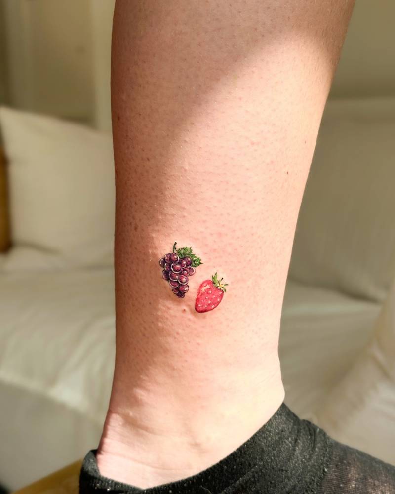 Illustrative style strawberry and grapes tattoo located on the ankle.