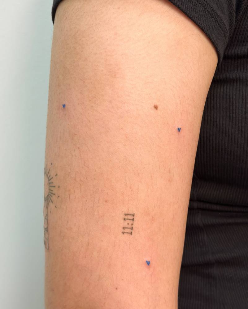 Minimalistic style micro blue hearts tattooed on the upper arm.