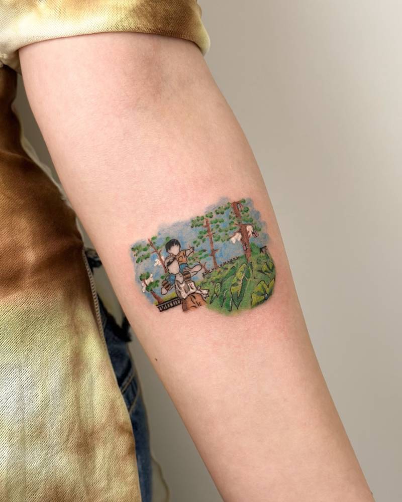 My Neighbor Totoro scene tattooed on the inner forearm in cartoon style.