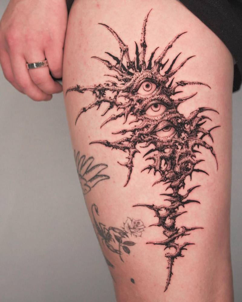 Eyes and thorns in illustrative style tattooed on the thigh.