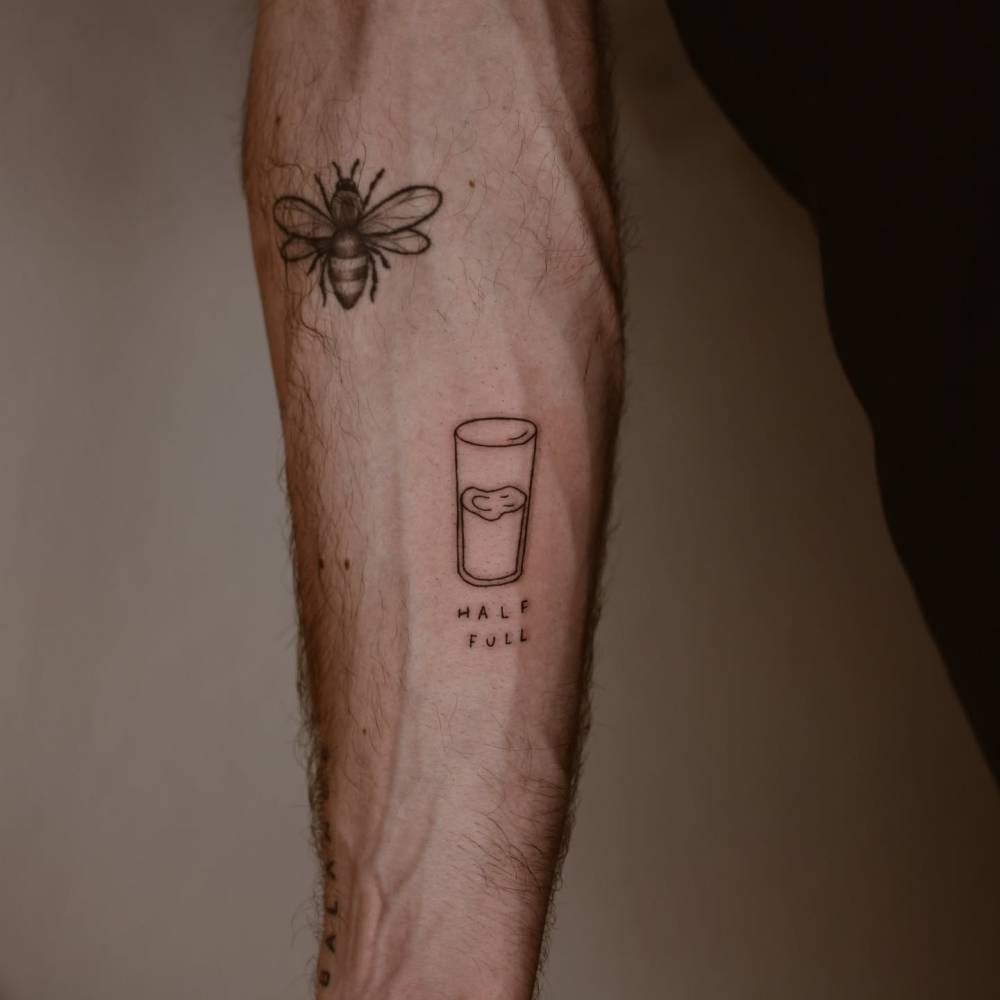 Glass half full tattoo located on the inner forearm.