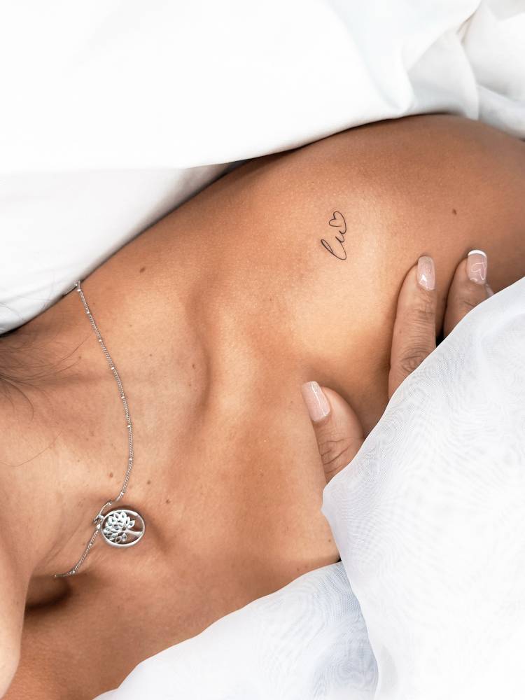 Initials and heart tattoo located on the shoulder, minimalistic style.
