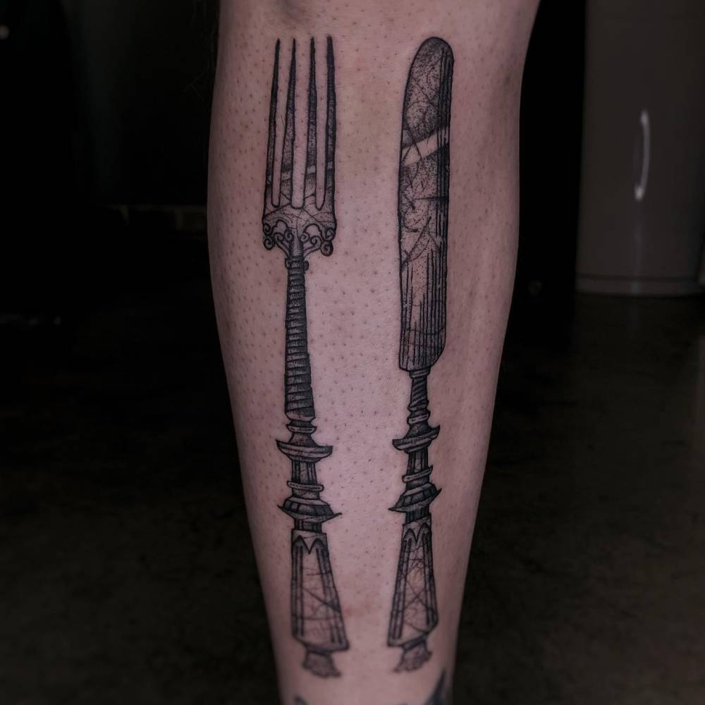 Engraving style knife and fork tattoo located on the shin.