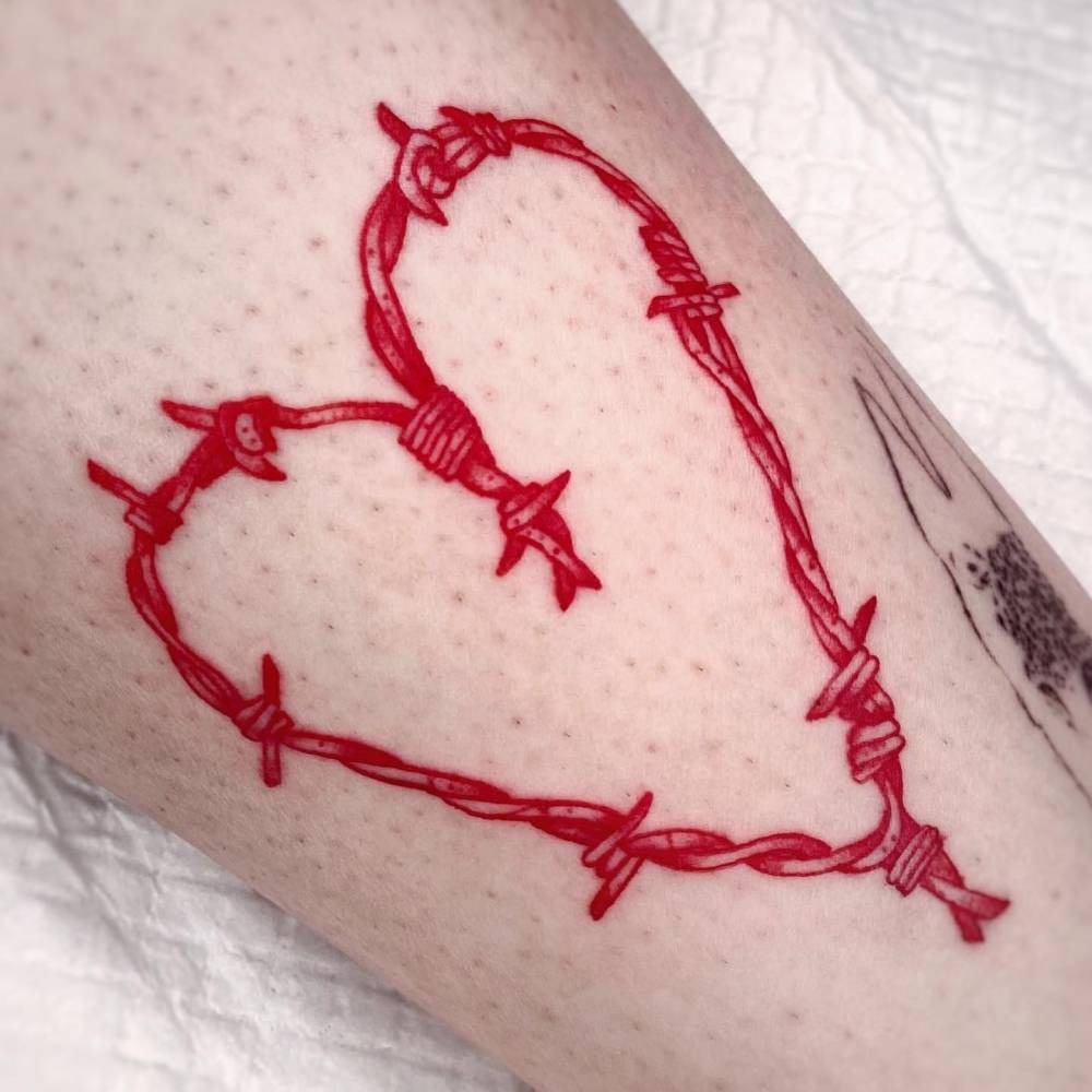 Red barbed wire heart tattoo located on the shin.