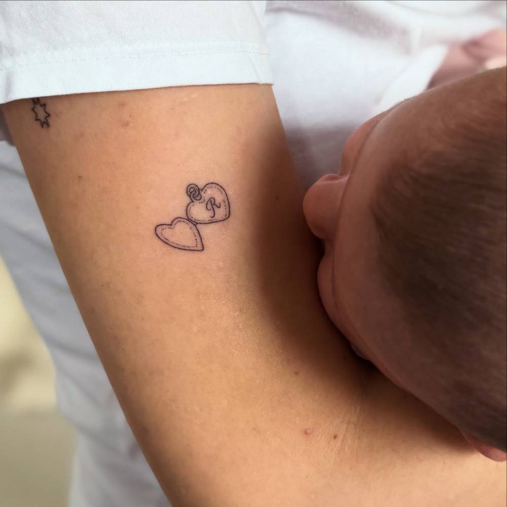 Hand poked heart pendant with the letter "R" tattoo located on the upper arm.
