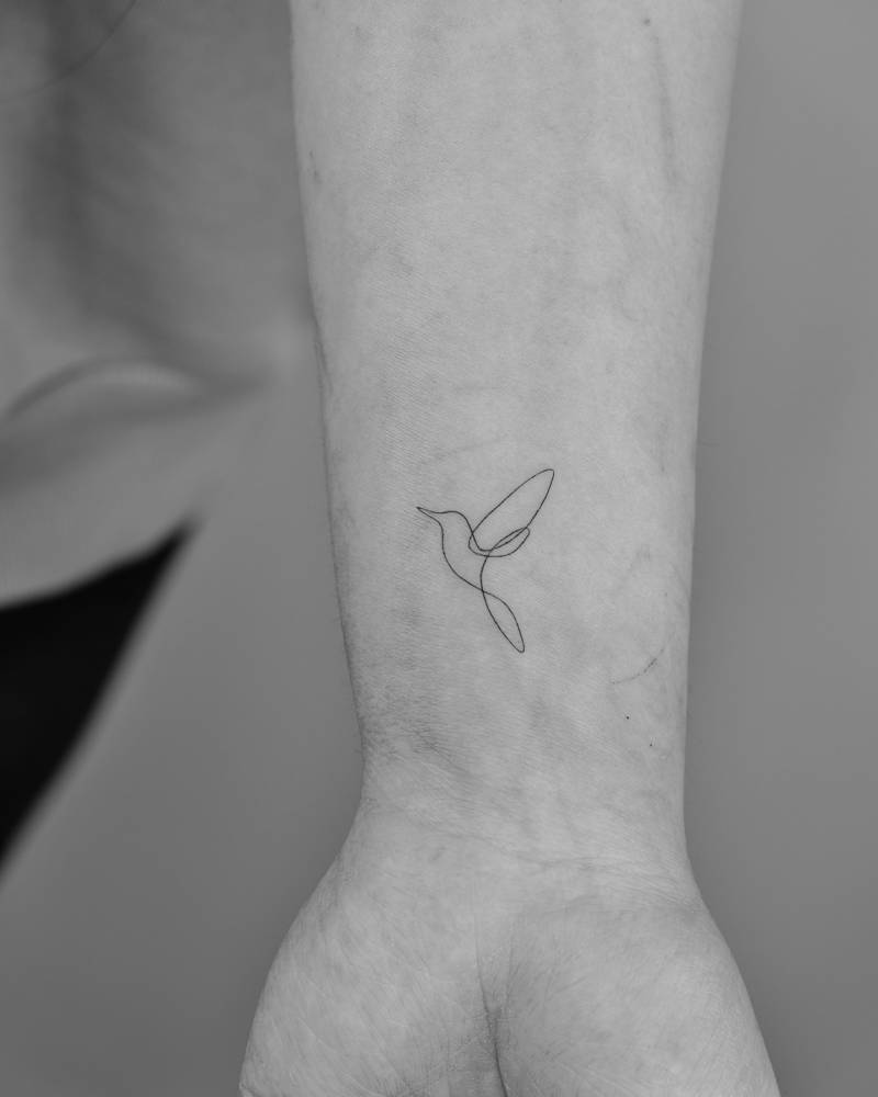 One line hummingbird tattoo located on the wrist.