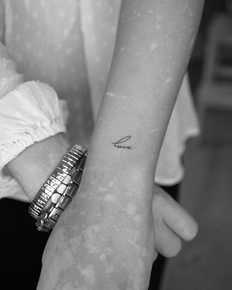 Handwritten font word "love" tattooed on the wrist.