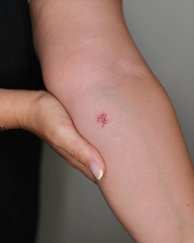 Chinese character tattoo in red ink located on the inner forearm.