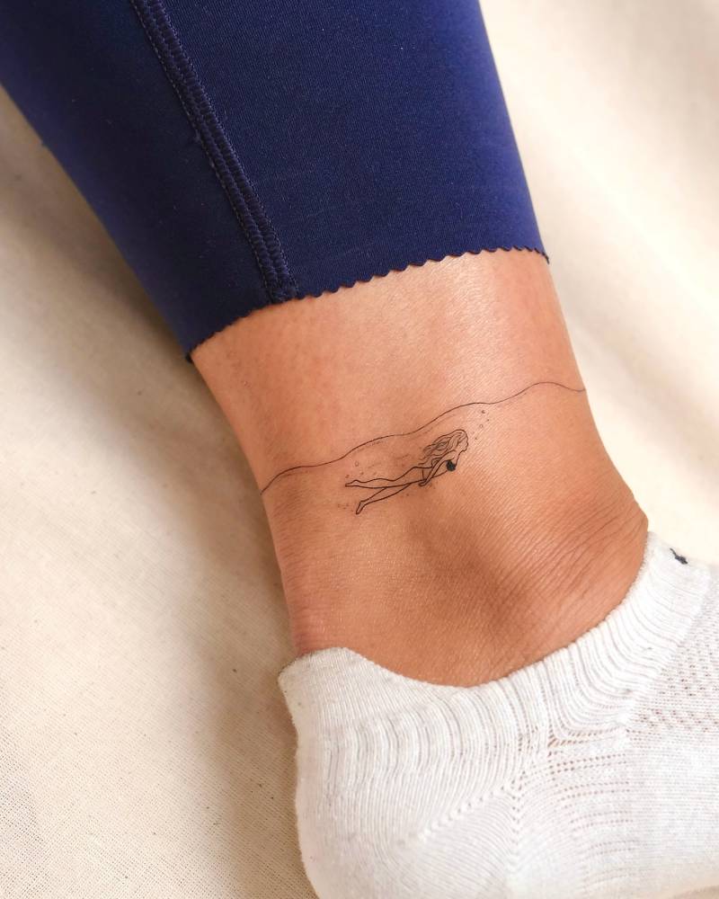 Fine line style little swimmer tattoo located on the ankle.