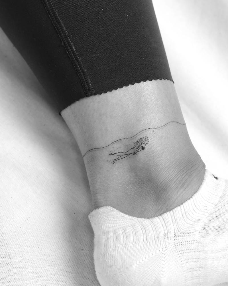 Fine line style little swimmer tattoo located on the ankle.