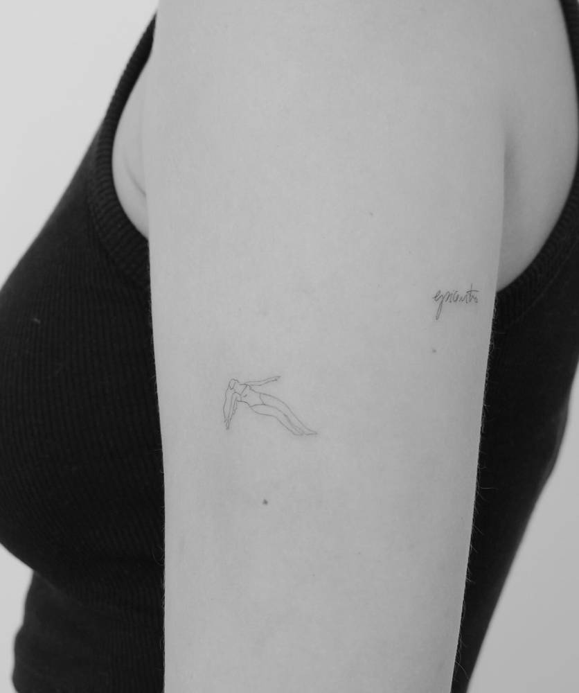 Fine line style swimmer tattoo located on the upper arm.