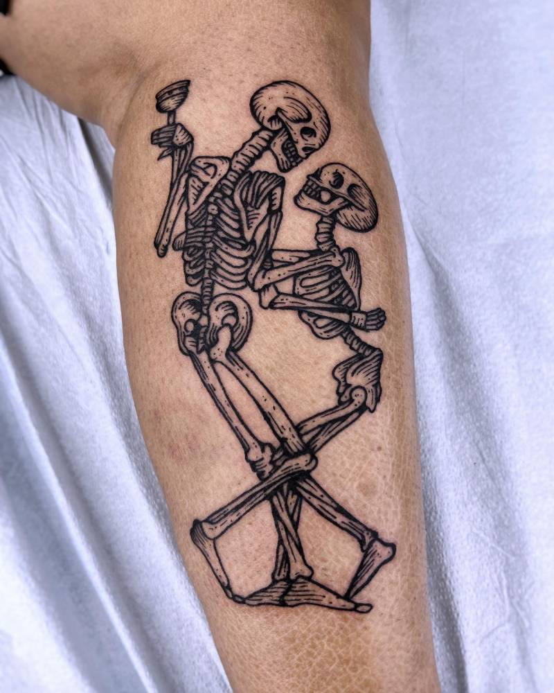 Dancing skeletons tattoo in blackwork style located on the shin.