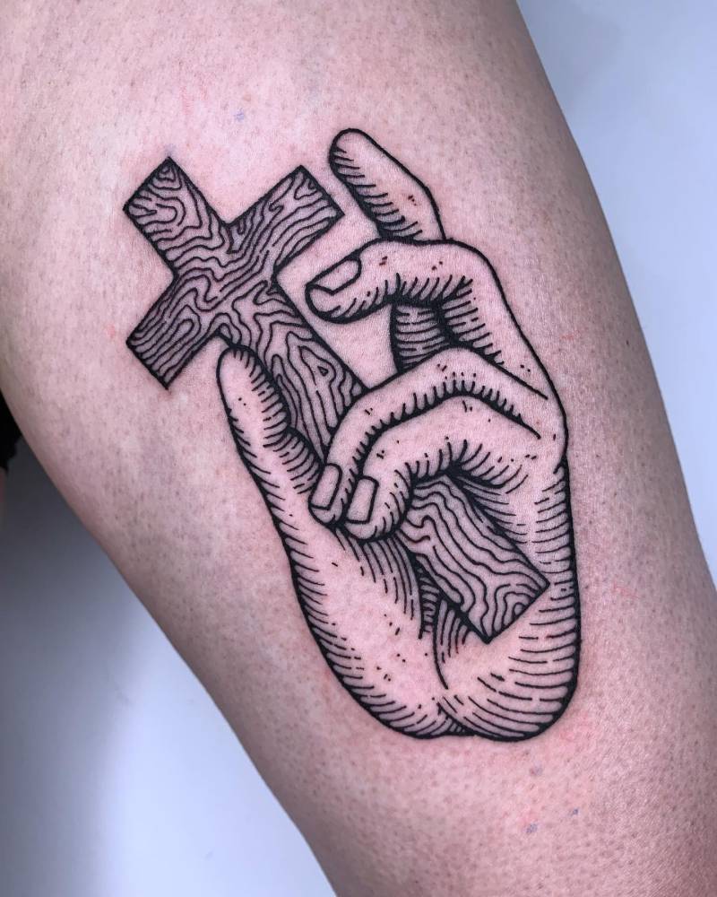 Hand holding cross tattoo in blackwork style done on the thigh.