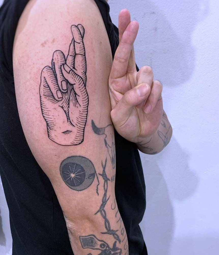 Engraving style crossed fingers tattoo located on the upper arm.
