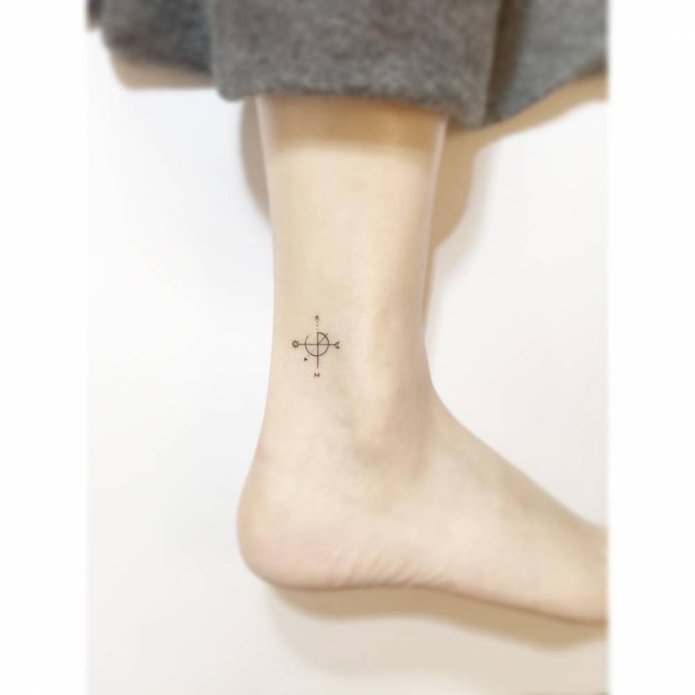 Compass rose tattoo in minimalistic style located on the ankle.