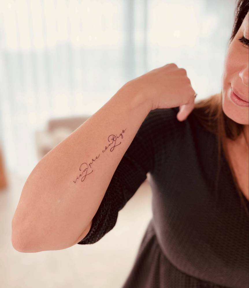 "Siempre contigo" lettering tattoo in handwritten font placed on the forearm.