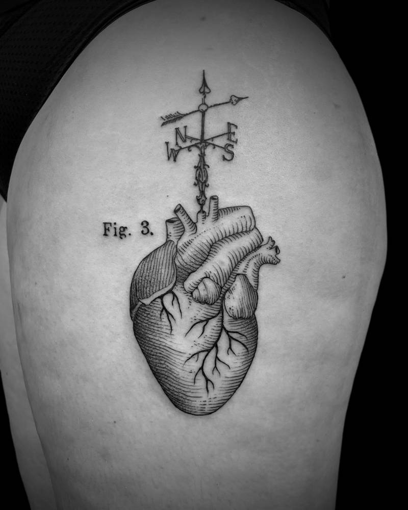 Anatomical heart and compass rose tattoo in engraving style located on the thigh.