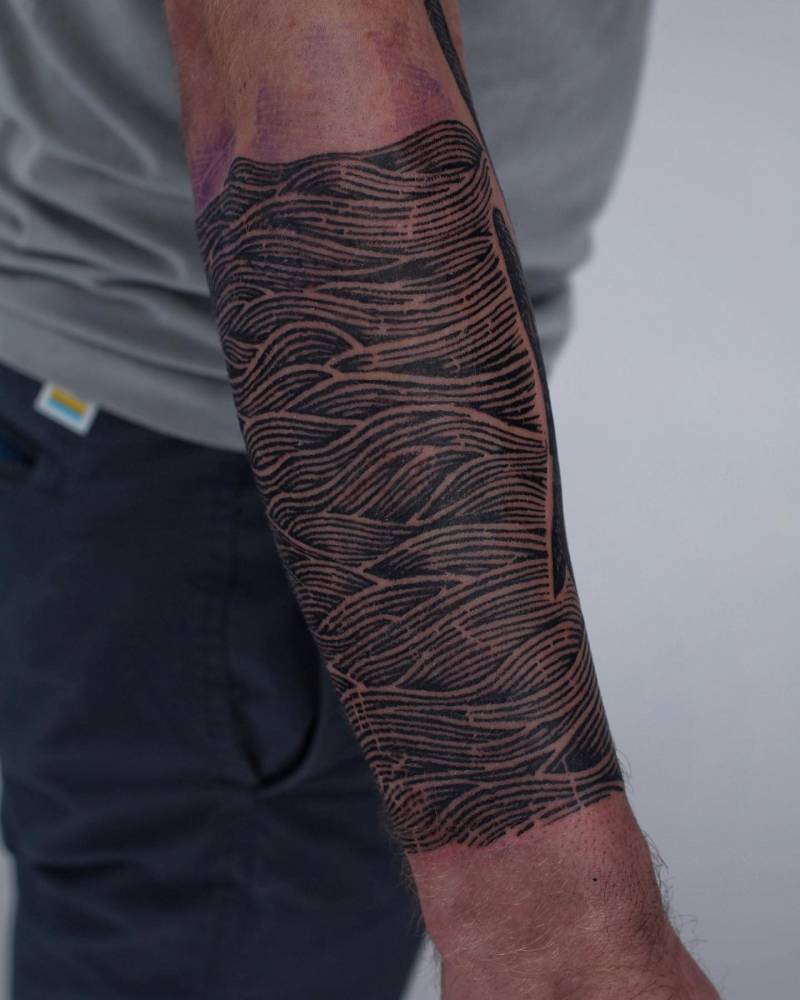 Engraving style waves tattoo located on the forearm.
