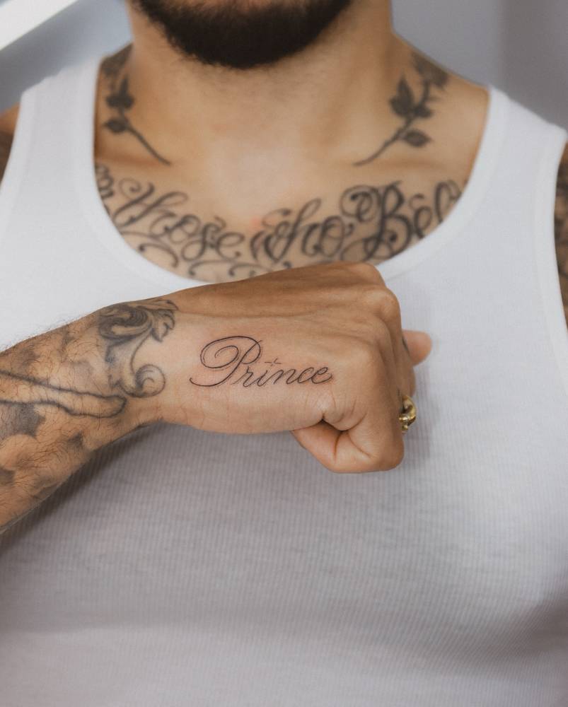 Lettering tattoo of the name "Prince" located on the hand.