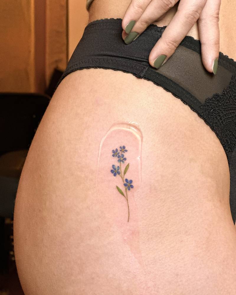 Watercolor style forget-me-not flowers tattoo located on the hip.