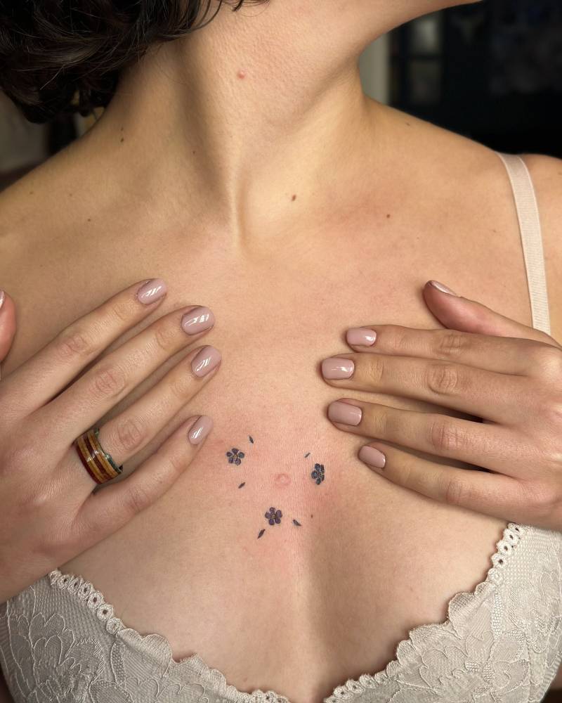 Little forget-me-not flowers tattooed on the sternum, watercolor style.