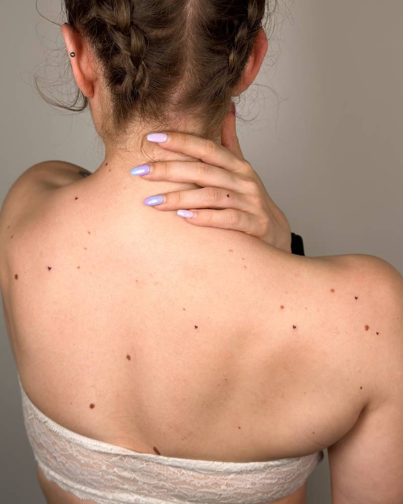 Heart freckles tattooed on the upper back, minimalistic style.