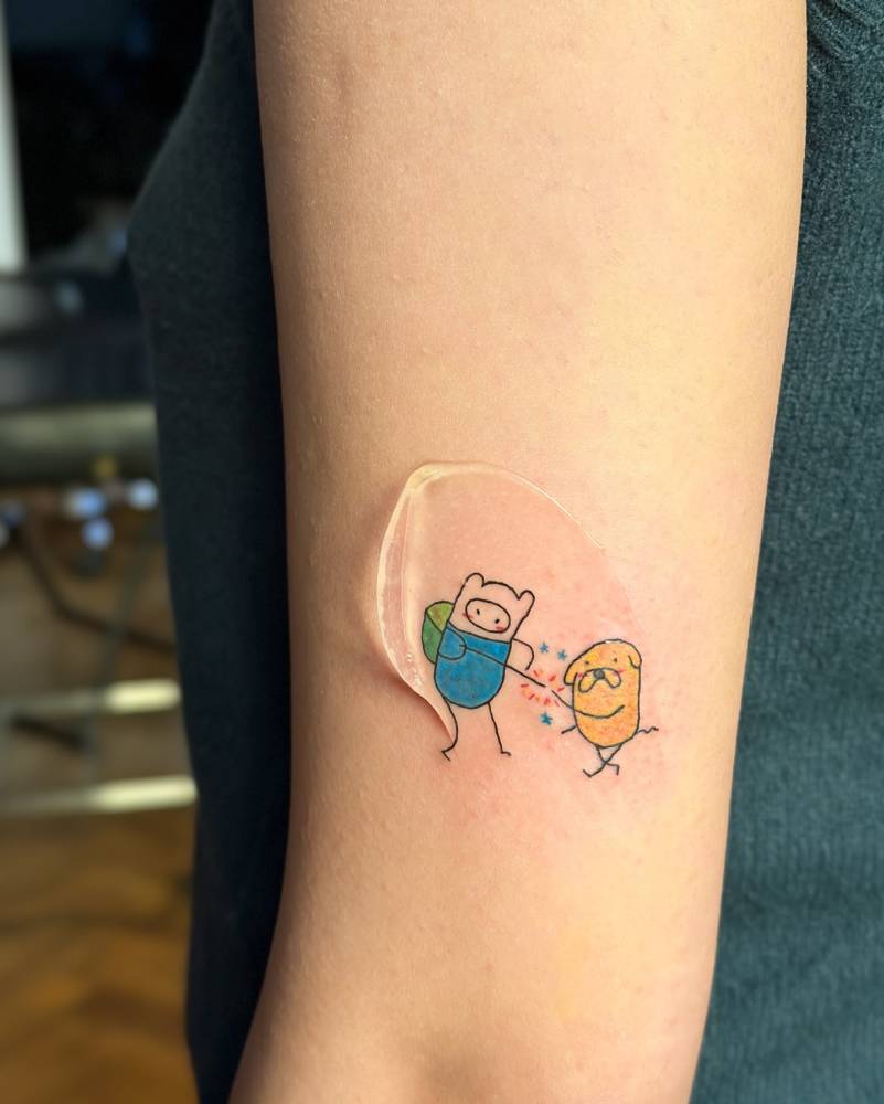 Finn and Jake tattoo in cartoon style placed on the upper arm.