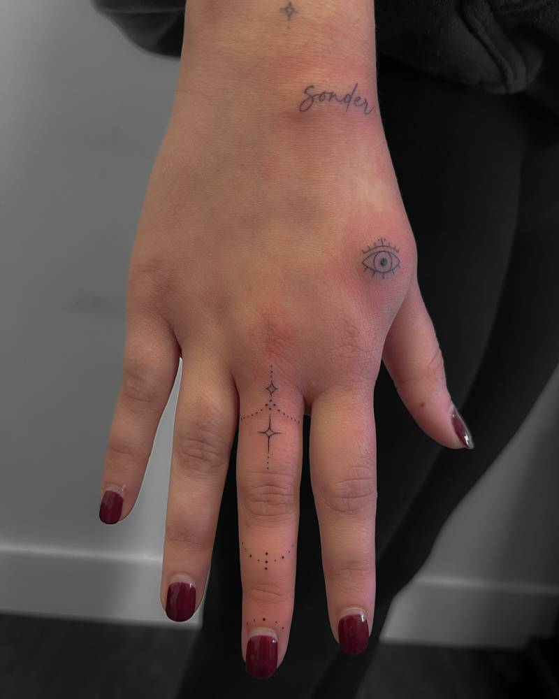 Word "sonder", evil eye and ornament tattooed on the hand and wrist.