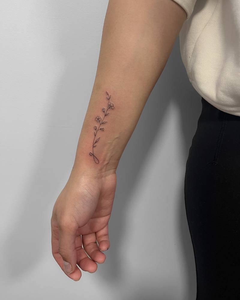 Letter "G" and flowers tattoo located on the wrist, fine line style.