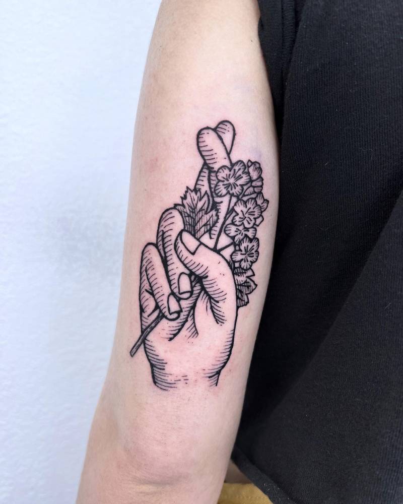 Crossed fingers tattoo located on the tricep, done in engraving style.