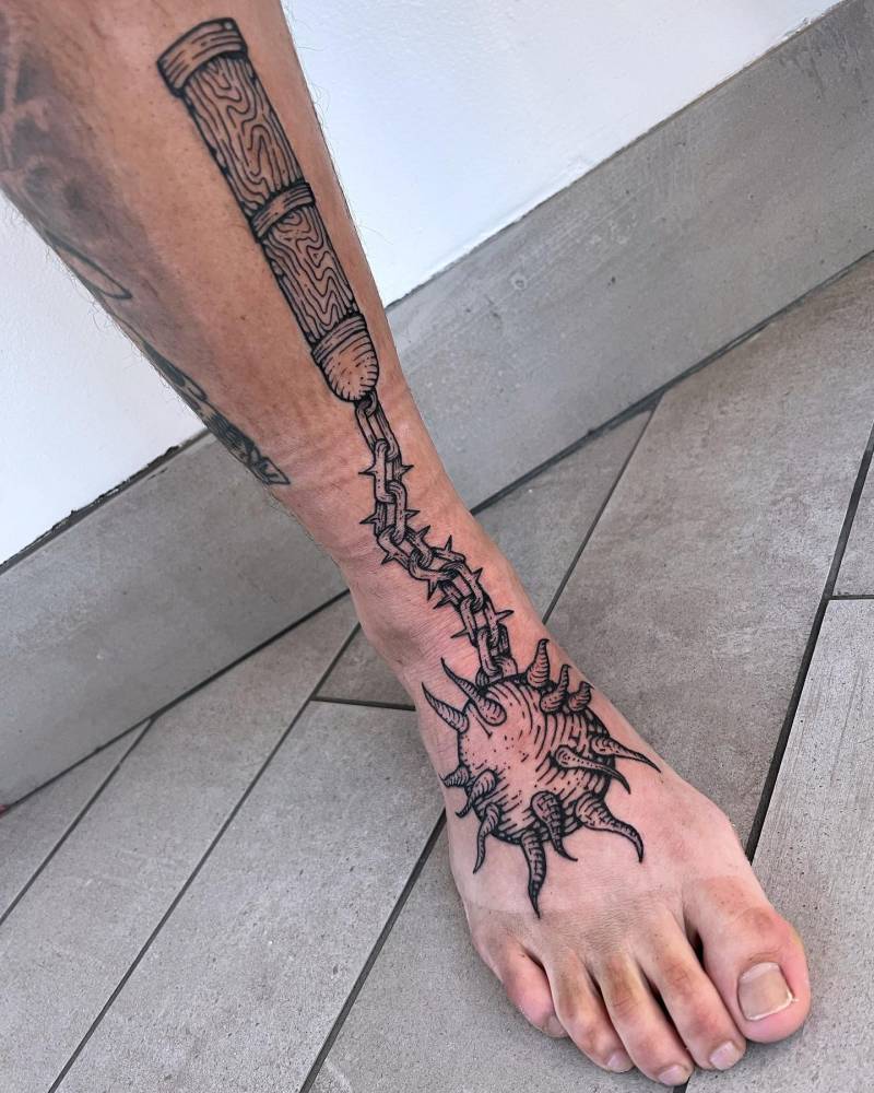 Flail tattoo in engraving style located on the shin and foot.