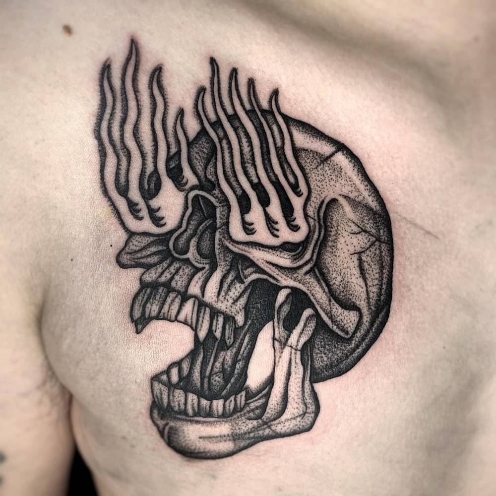 Flaming skull tattoo placed on the chest, blackwork style.