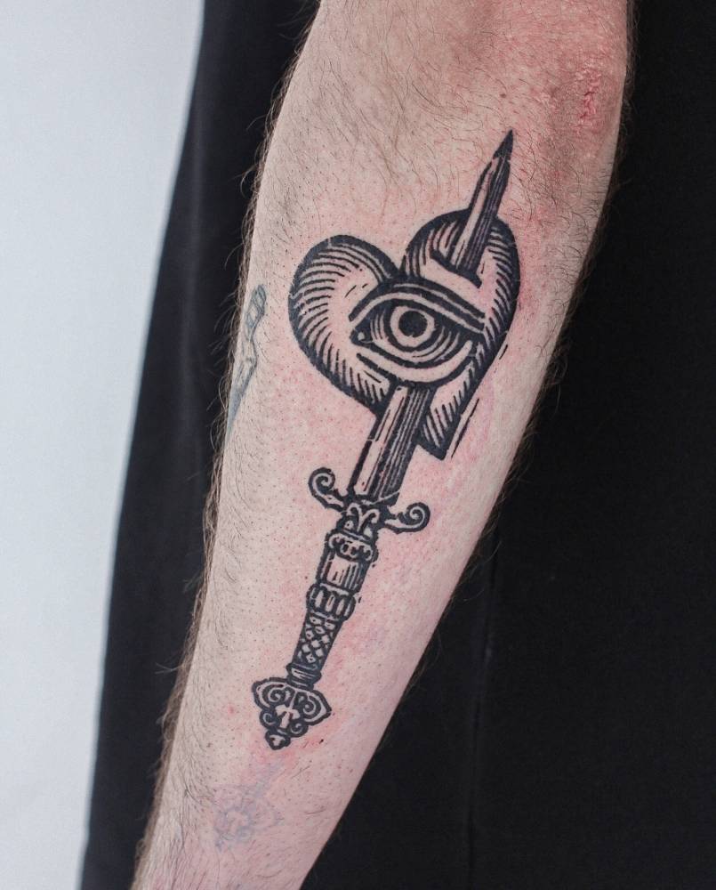 Engraving style heart and dagger tattoo located on the forearm.
