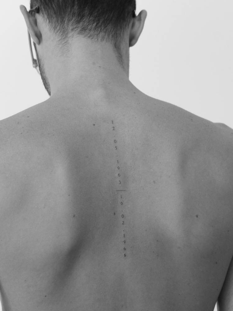 Dates tattoo in serif font placed on the spine.