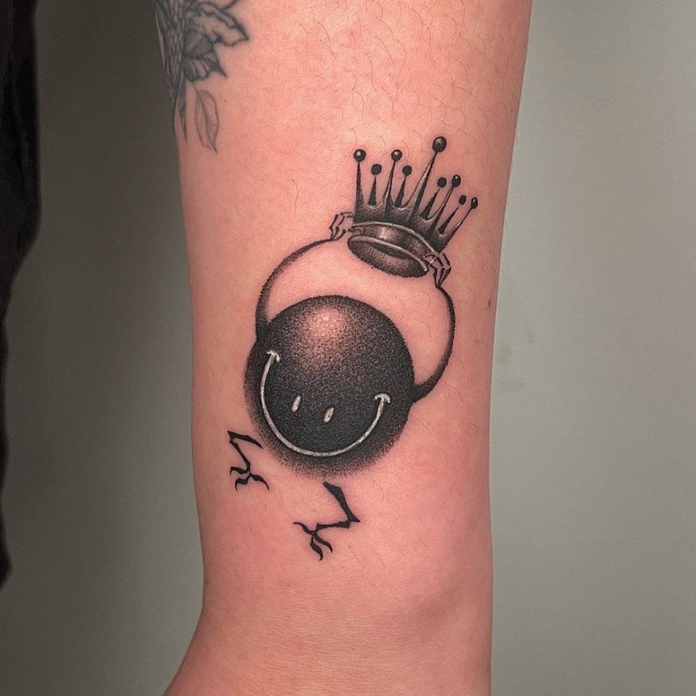Smiley and crown tattoo in dotwork style located on the wrist.