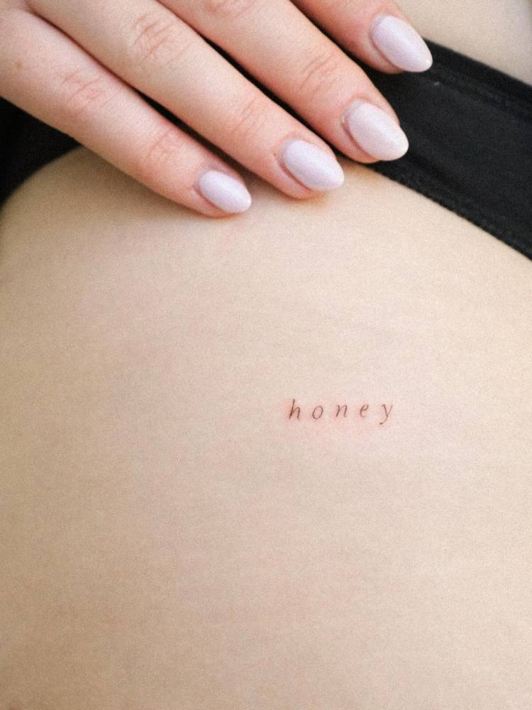 Lettering tattoo of the word "honey" in serif font placed on the rib.