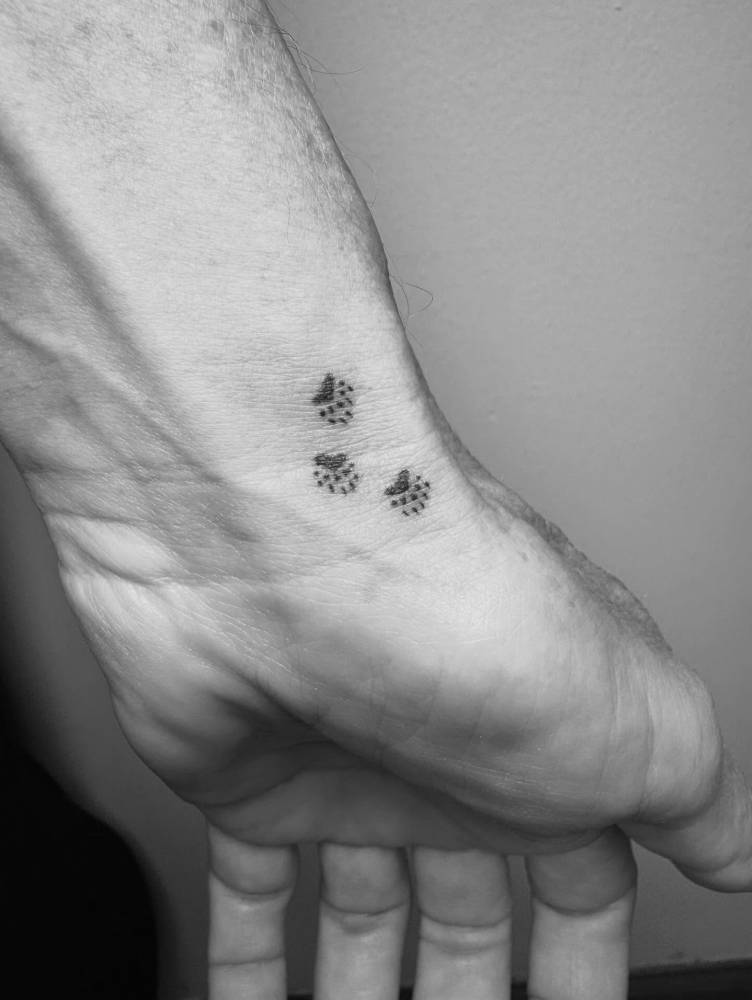 Minimalistic style paw prints tattoo located on the wrist.
