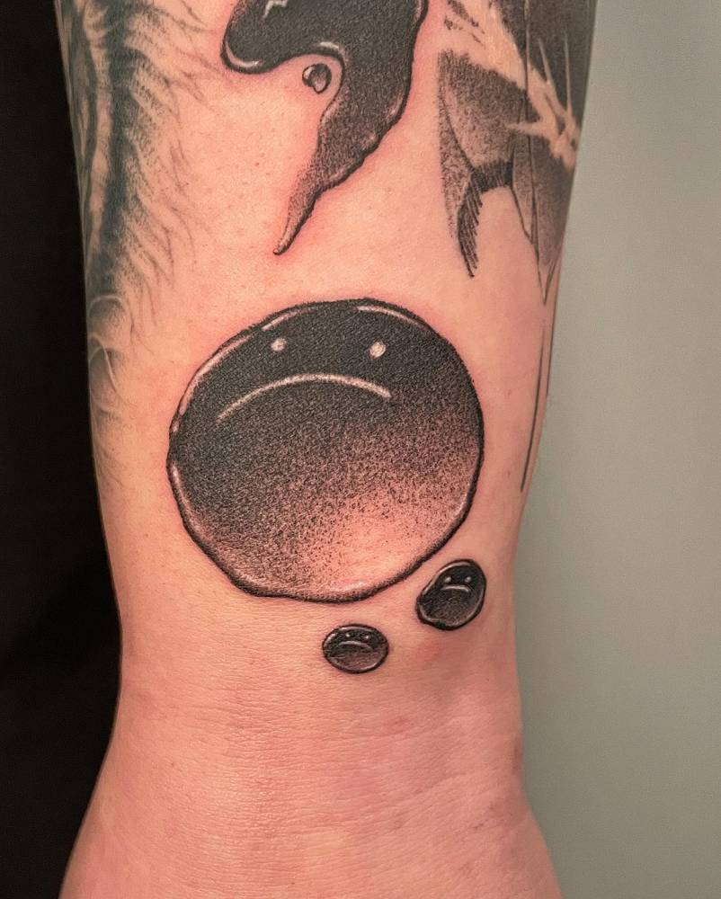 Sad face tattoo in dotwork style located on the wrist.