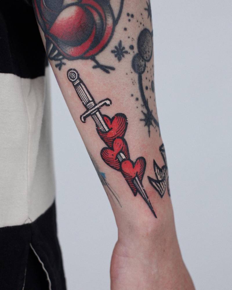 Pop art style heart and dagger tattoo located on the wrist.