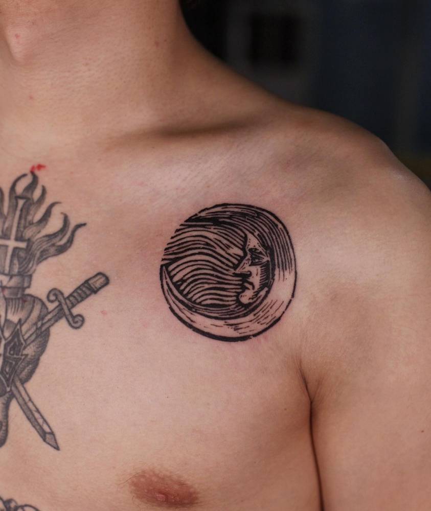 Engraving style moon face tattoo located on the shoulder.