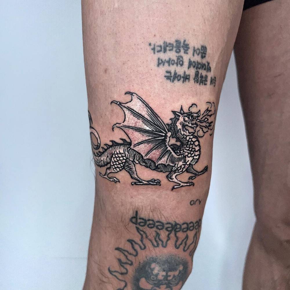 Dragon tattoo in cartoon style located on the thigh.