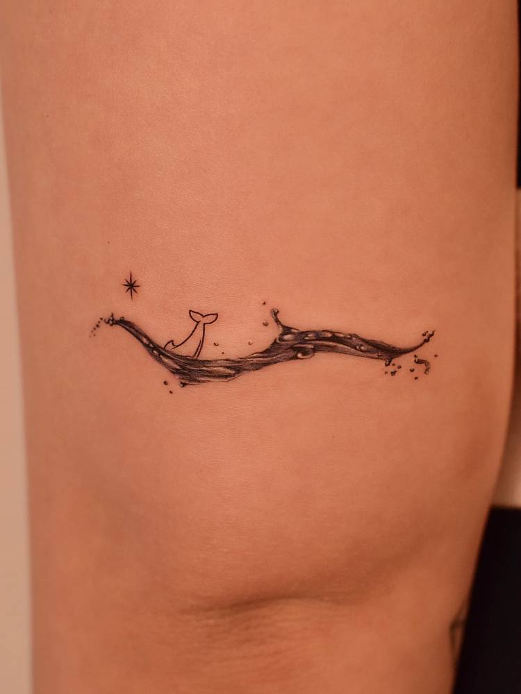 Dolphin and waves tattoo in illustrative style located on the tricep.