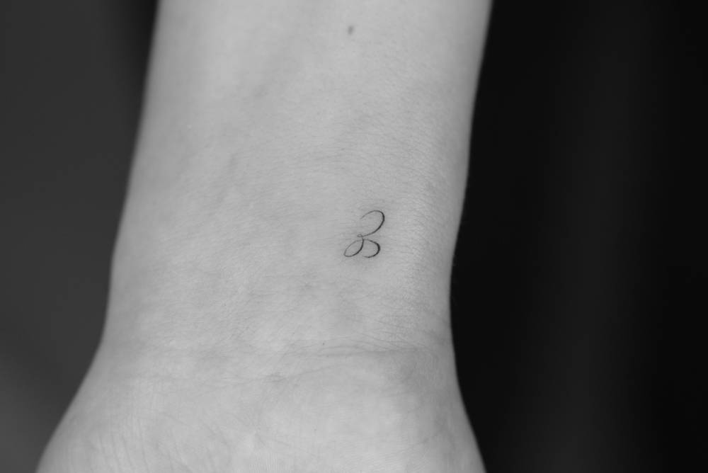 Script font letter "E" tattoo placed on the wrist.