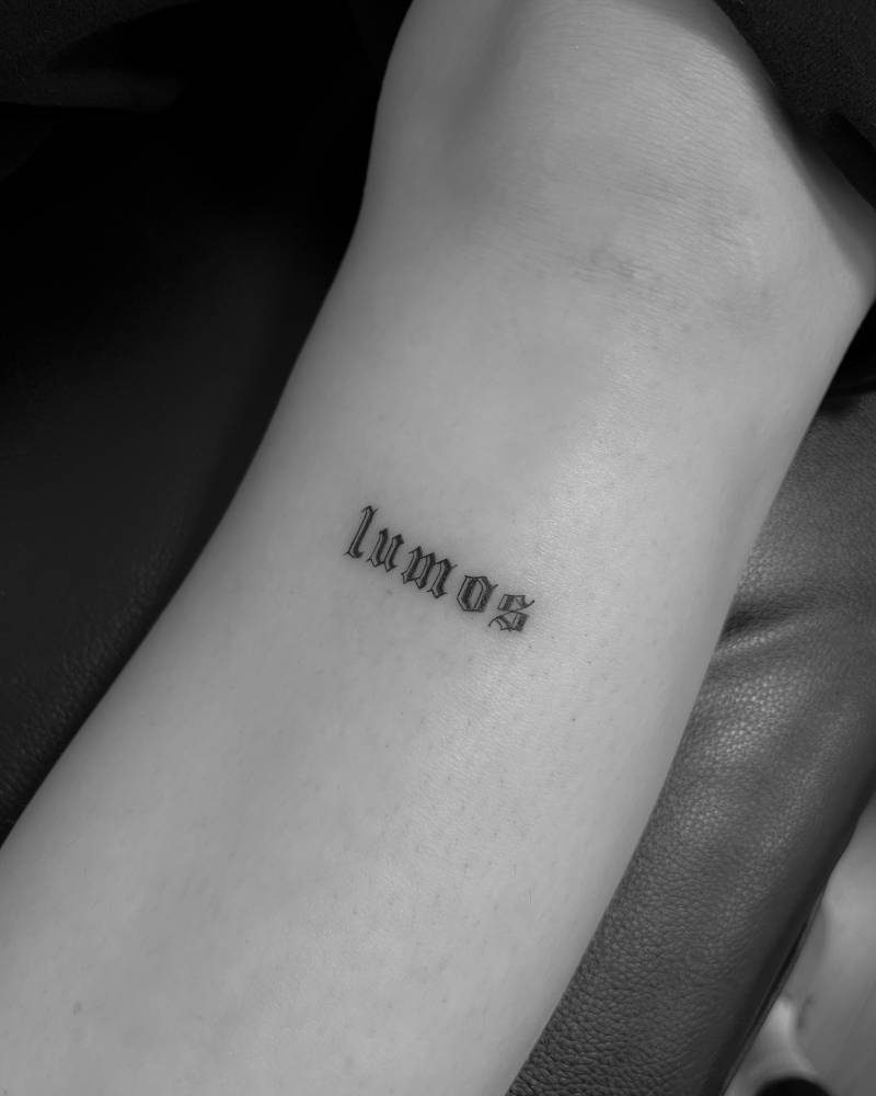 "Lumos" lettering tattoo in gothic font located on the shin.