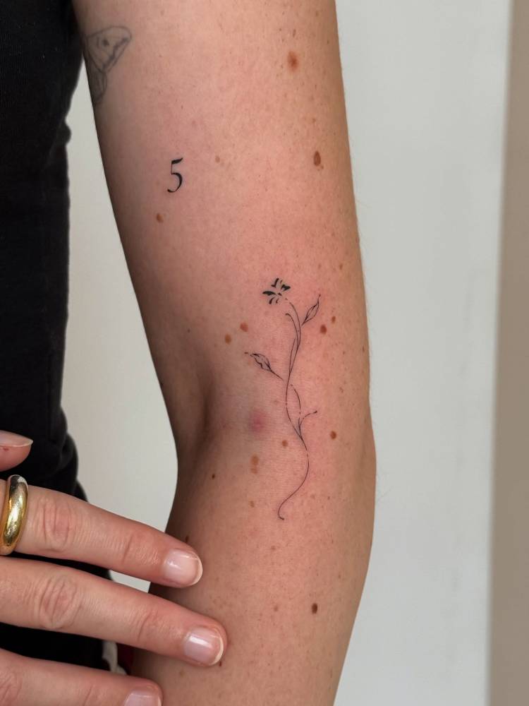 Fine line style ornamental flower tattoo located on the elbow.