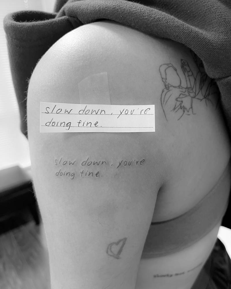 Handwritten font "slow down, you're doing fine" tattoo located on the upper arm.