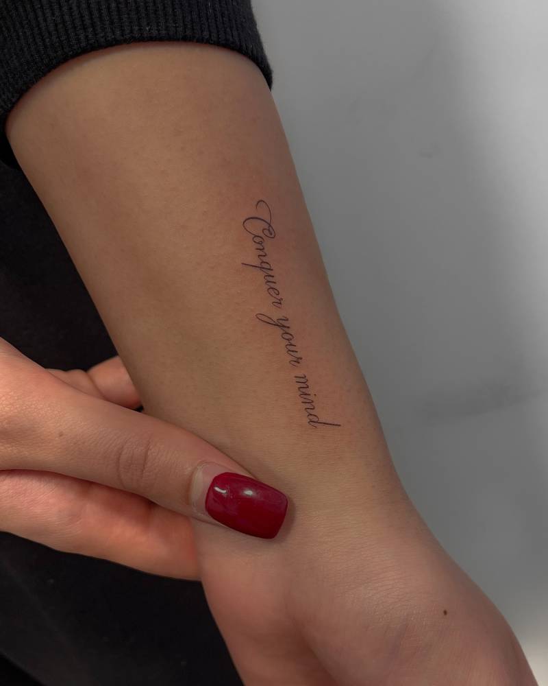 "Conquer your mind" lettering tattoo placed on the wrist.