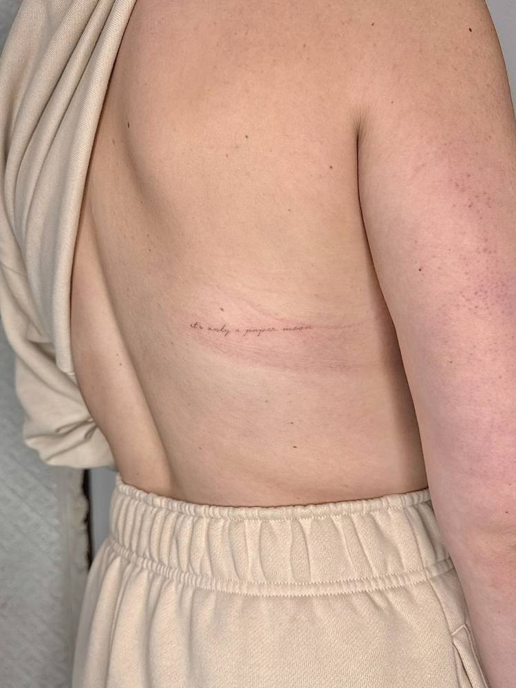 "It's only a paper moon" lettering tattoo handwritten on the back.